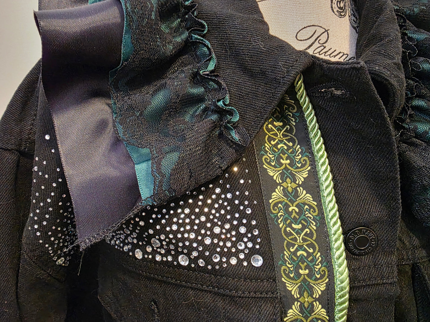 Close-up of a dark coat with decorative elements including ribbons and embroidery.