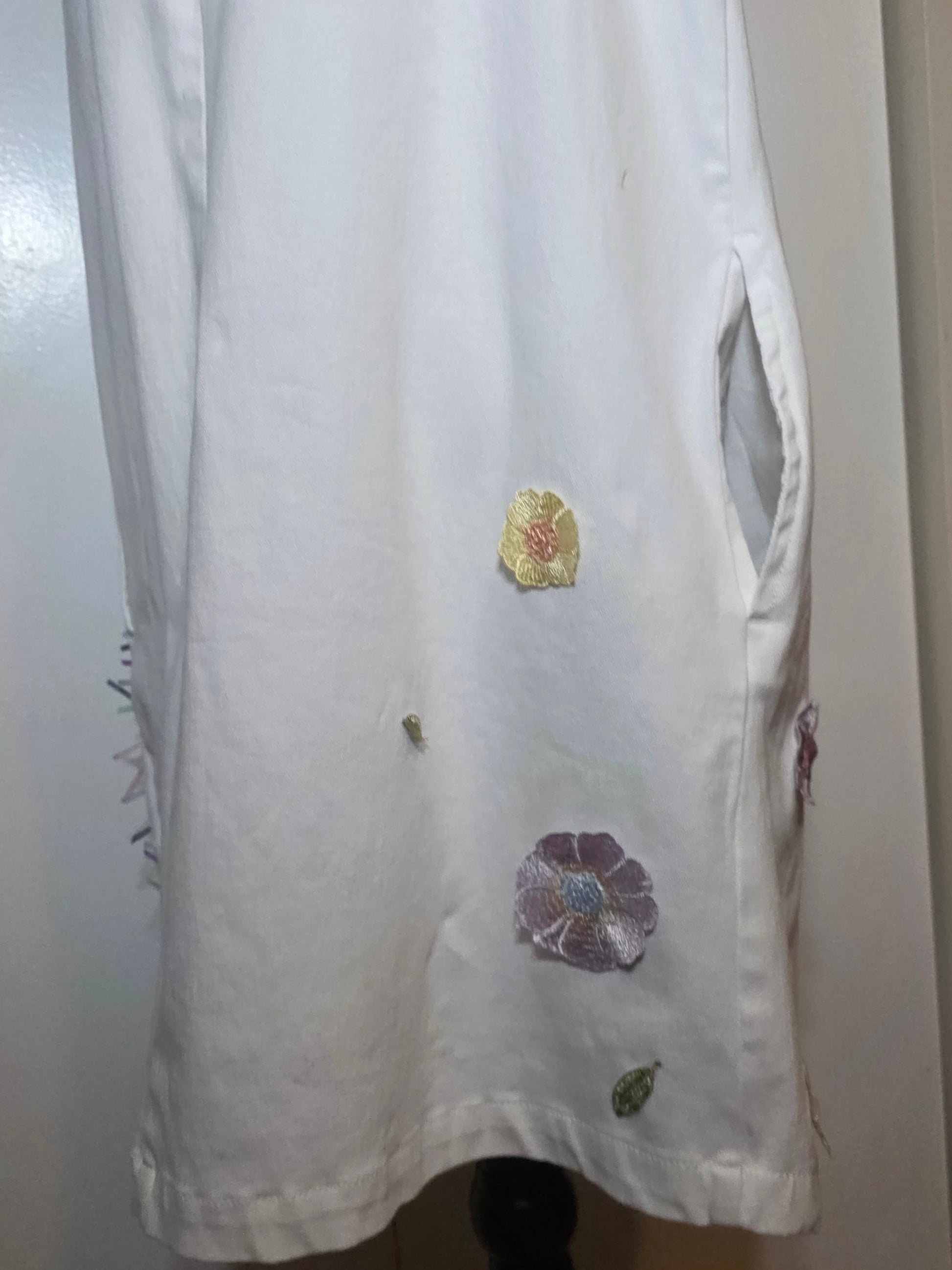 White denim sleeveless dress hand embellished with line-art woman, dimensional embroidered flowers and cascading pastel satin ribbons, with pockets.