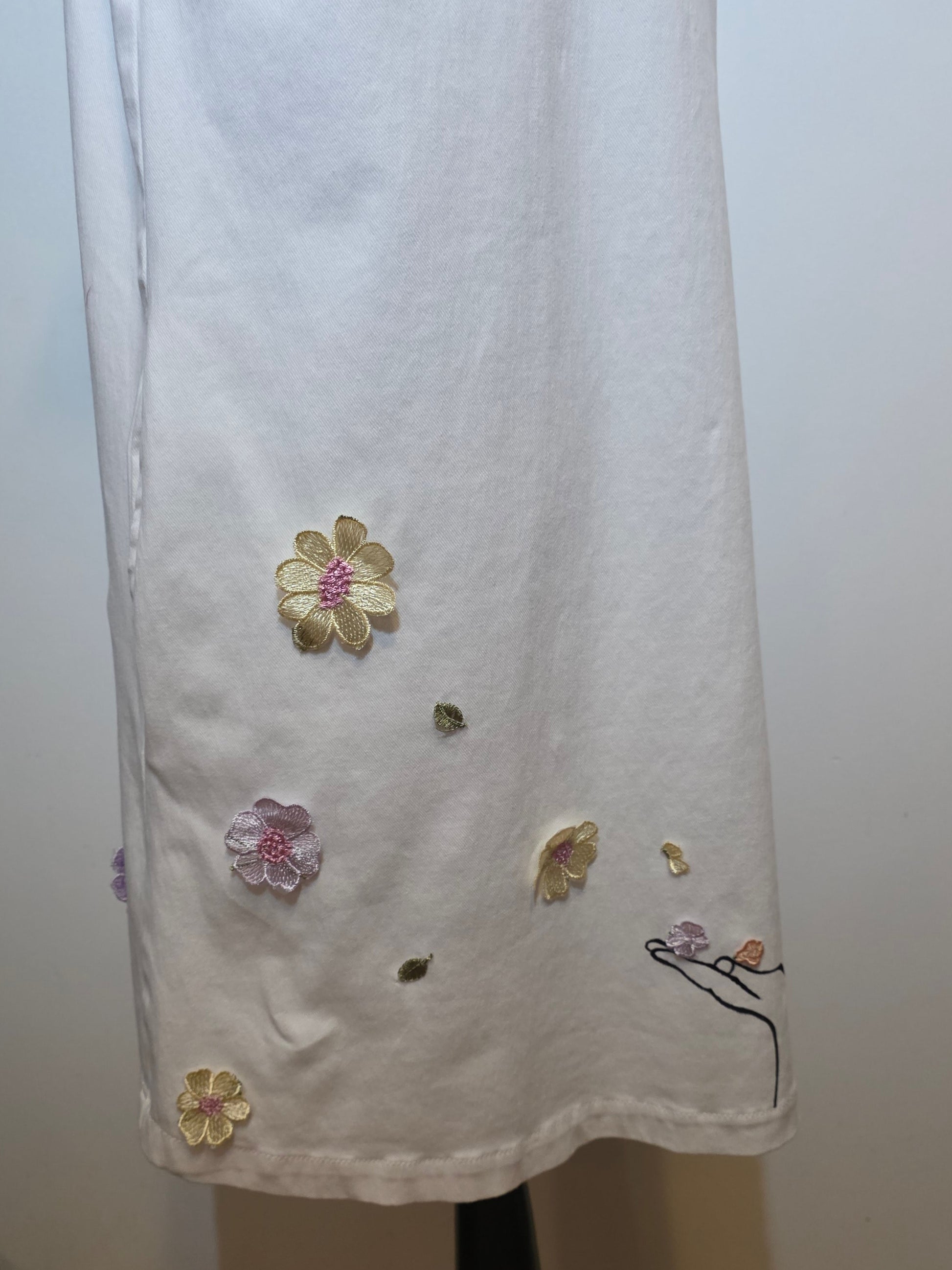 White denim sleeveless dress hand embellished with line-art woman, dimensional embroidered flowers and cascading pastel satin ribbons.